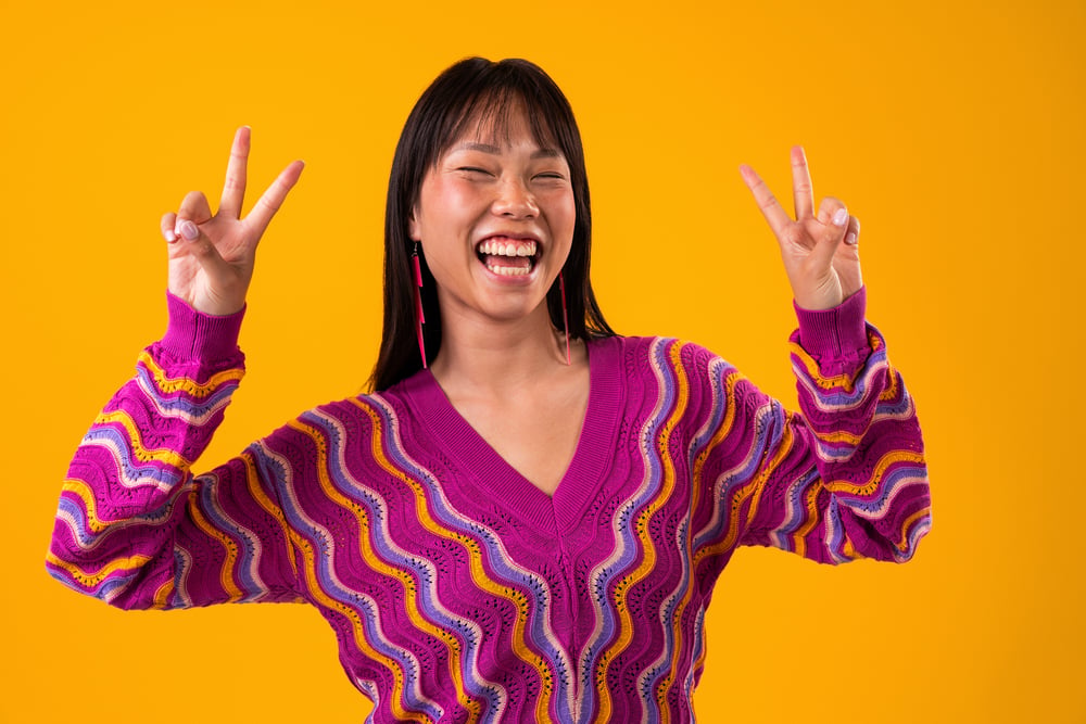 smiling-woman-with-peace-sign-on-yellow-background-2026-03-09-02-51-16-utc